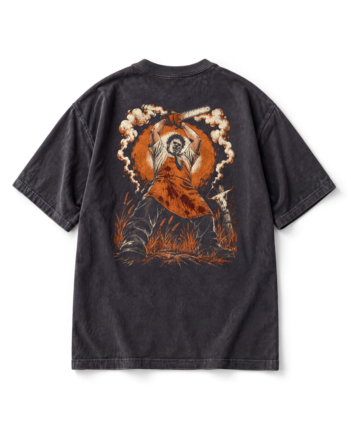 Back print: Leatherface in an apron swinging a chainsaw overhead against a big orange sun, smoke curling round.